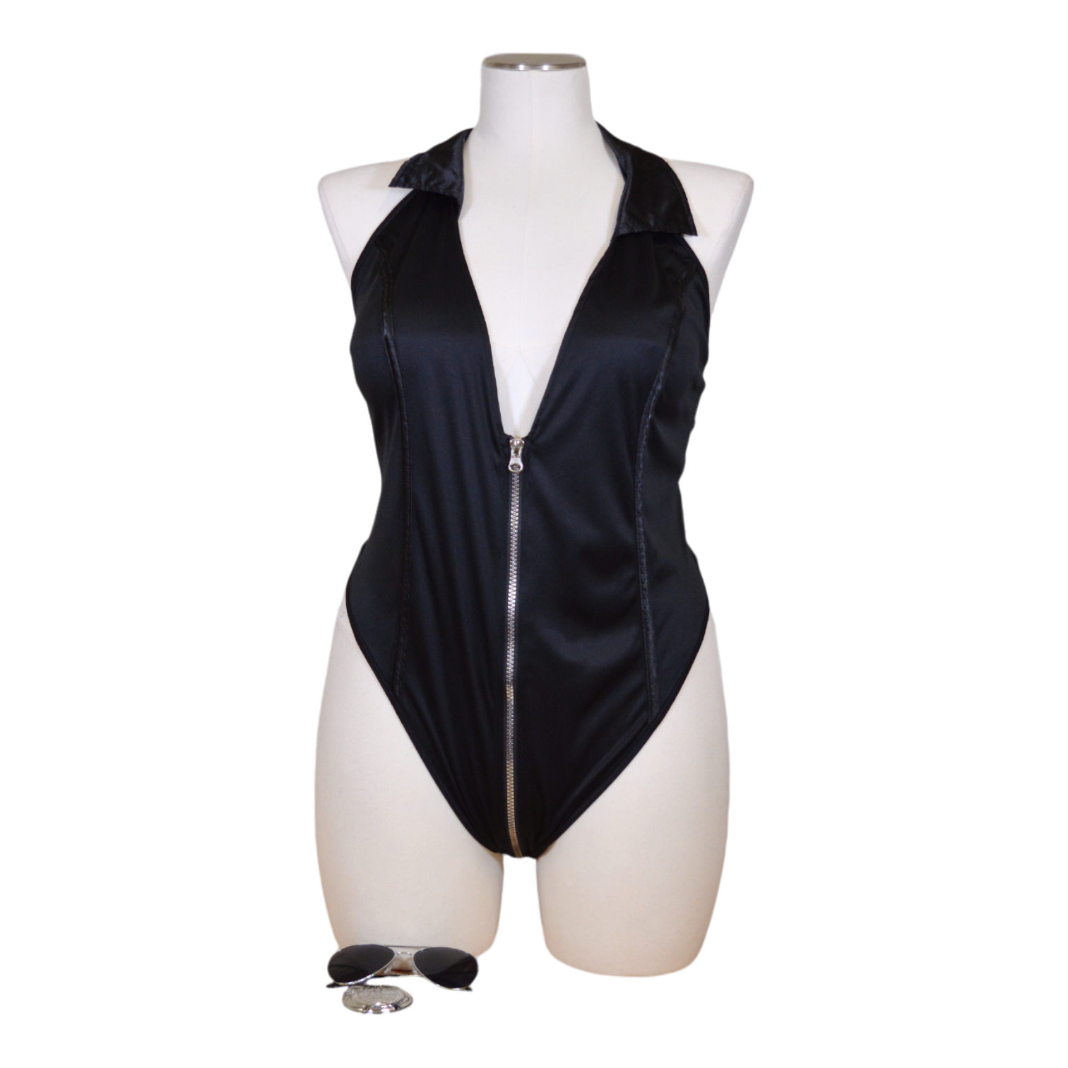 A black bodysuit with a front and back zipper, collar, and additional accessories such as glasses and a badge displayed on a mannequin.