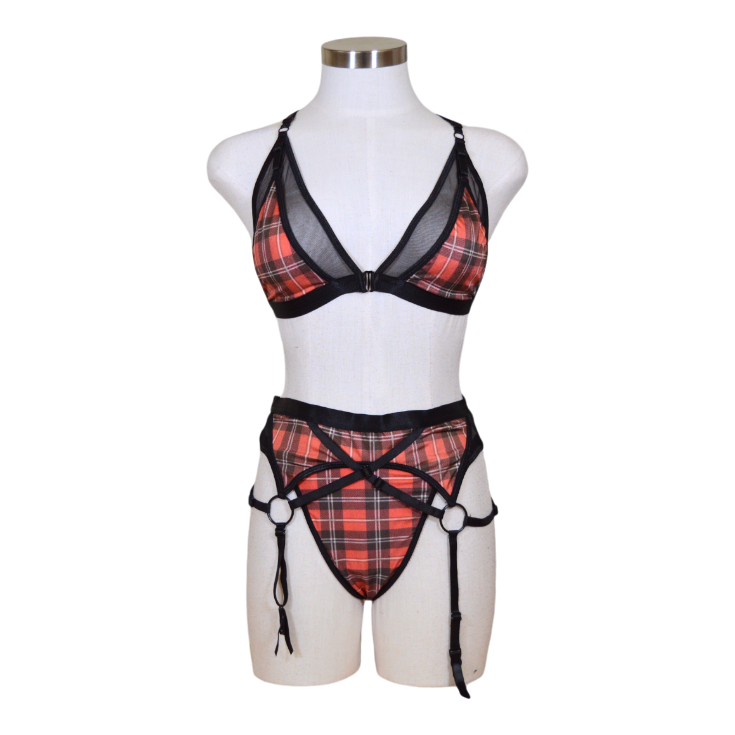 This image features a seductive 3-piece lingerie set displayed on a mannequin, highlighting a bold red and black plaid pattern. The set includes a strikingly designed bra with adjustable straps and mesh accents, a matching garter belt with similar plaid and mesh detailing, and coordinating panties that complement the bra and garter belt.